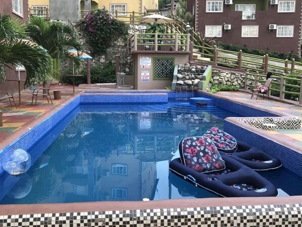 Relax by the rectangular pool surrounded by lush greenery and a traditional building backdrop.