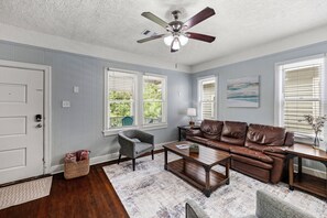 A living room with a ceiling fan, a brown leather sofa, a gray armchair, a coffee table, and a wicker basket.