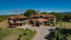 Uma casa moderna e espaçosa de dois andares, com um amplo jardim frontal, varanda coberta e vista para a paisagem ao redor.