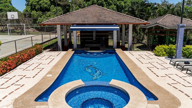 Piscina com hidromassagem, cercada por um pavilhão coberto e uma quadra de basquete.