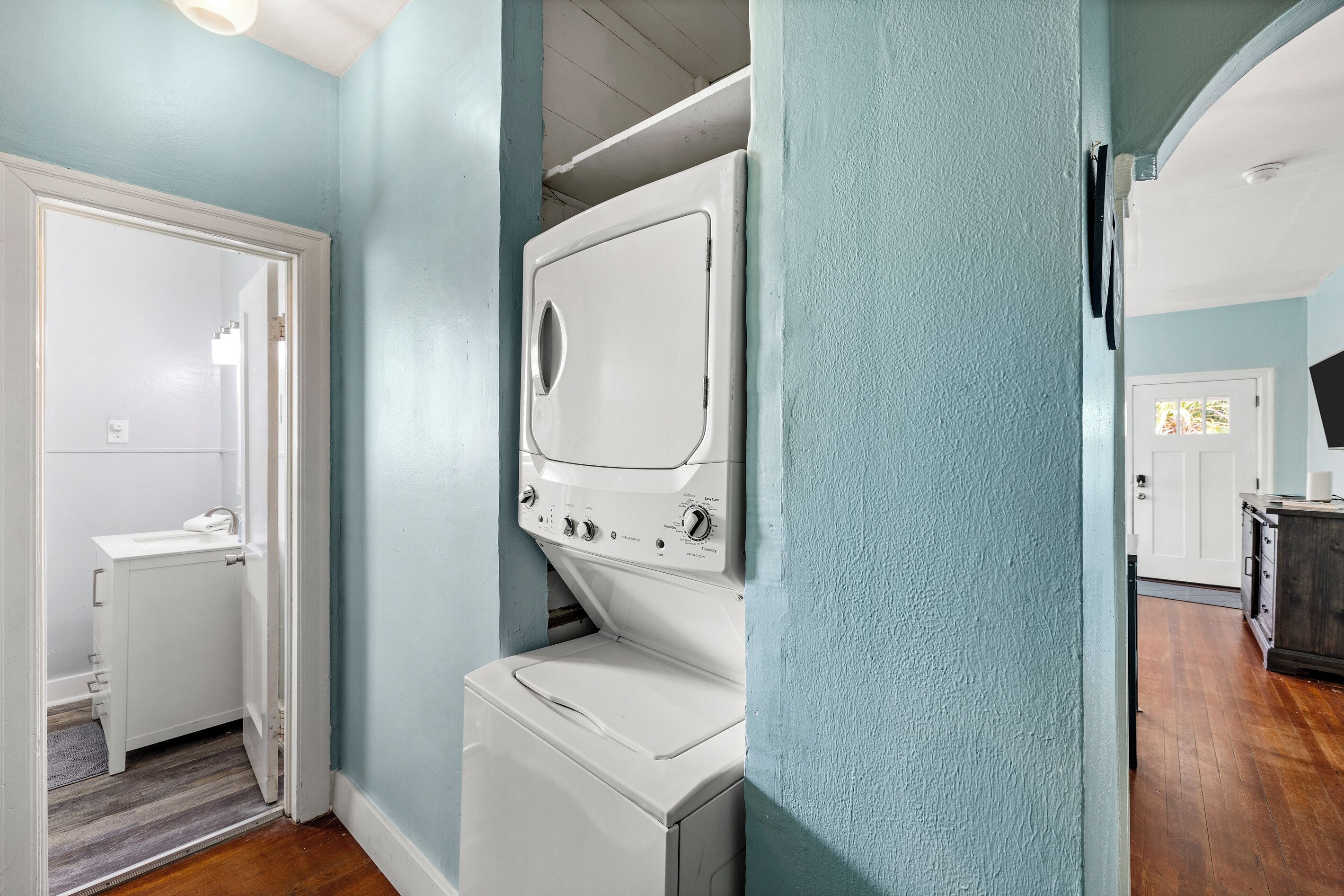 A laundry room with a washer and dryer, a small bathroom with a toilet, and a door leading to another room.