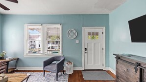 A room with a blue wall, a white door, a gray chair, a wooden table, and a small white basket. - The Starboard at M | Historic Lost Bayou Retreat • Walk to Beach • Sleeps 6 (Galveston)