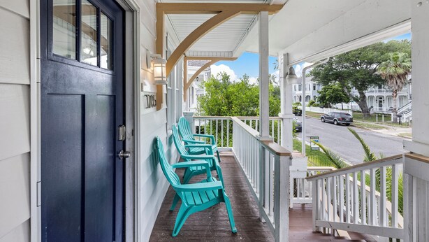 Eine Veranda mit einer schwarzen Tür, weißen Geländern und grünen Adirondack-Stühlen.