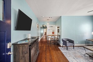 A hallway with a wooden floor, a blue door, a dark wooden cabinet, a table with stools, and a chair.