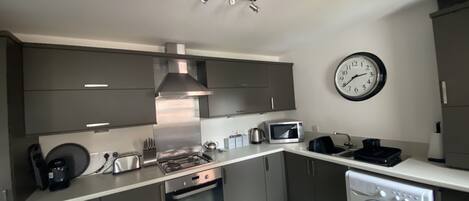 Una cocina moderna con gabinetes grises, una campana extractora de acero inoxidable, un microondas, un hervidor y una lavadora integrada.