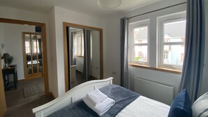 A bedroom with a bed, a mirror, a window, and a radiator. - Little Acorn - 2-bed Anstruther Apartment (Anstruther)