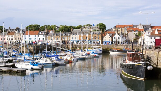 A harbor with multiple boats docked, a waterfront promenade, and buildings with red-tiled roofs. - Little Acorn - 2-bed Anstruther Apartment (Anstruther)