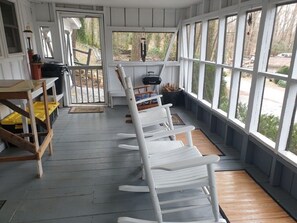 Relax on the porch with a view of lush surroundings, surrounded by comfortable seating and a dining area.