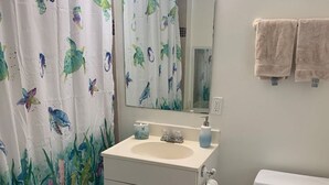 Een badkamer met een wit wastafel, een toilet, douchegordijn met zeedieren, en een spiegel boven het wastafel.