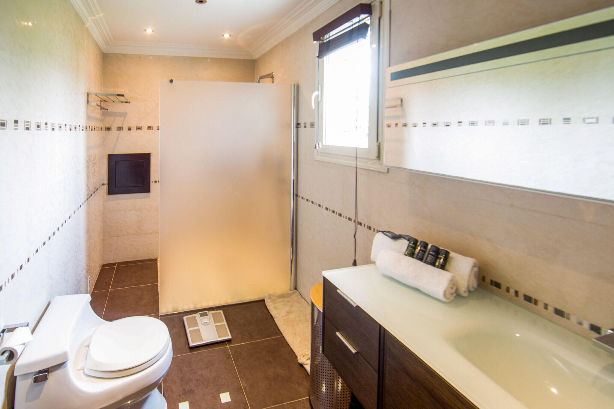 Un bagno con il water, una doccia, un lavandino con un asciugamano e una bilancia.