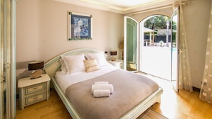 A bedroom with a bed, bedside tables, a nightstand, a window with a view, and a door leading to an outdoor area. - Family Villa with Pool & Leisure Activities (Antibes)