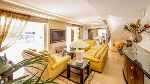 A modern living room with yellow sofas, a flat-screen TV, and a large window with curtains. - Family Villa with Pool & Leisure Activities (Antibes)