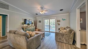 A spacious living room with two grey sofas, a wooden coffee table, a ceiling fan, and a large window offering a view of the outdoors. - Emerald Isle Escape: Walk to Ocean (Emerald Isle)