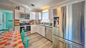 A modern kitchen with stainless steel appliances, white cabinetry, and a teal dining table. - Emerald Isle Escape: Walk to Ocean (Emerald Isle)