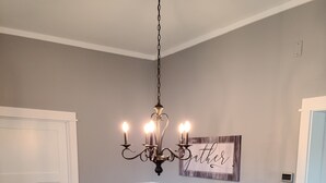 A dining room with a wooden table, white chairs, a chandelier, and a wall sign. - Fully renovated 3 bed, 2 bath home (Grand Marais)