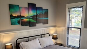 A bedroom with a bed, two bedside lamps, a ceiling fan, and three wall-mounted paintings. - Fully renovated 3 bed, 2 bath home (Grand Marais)