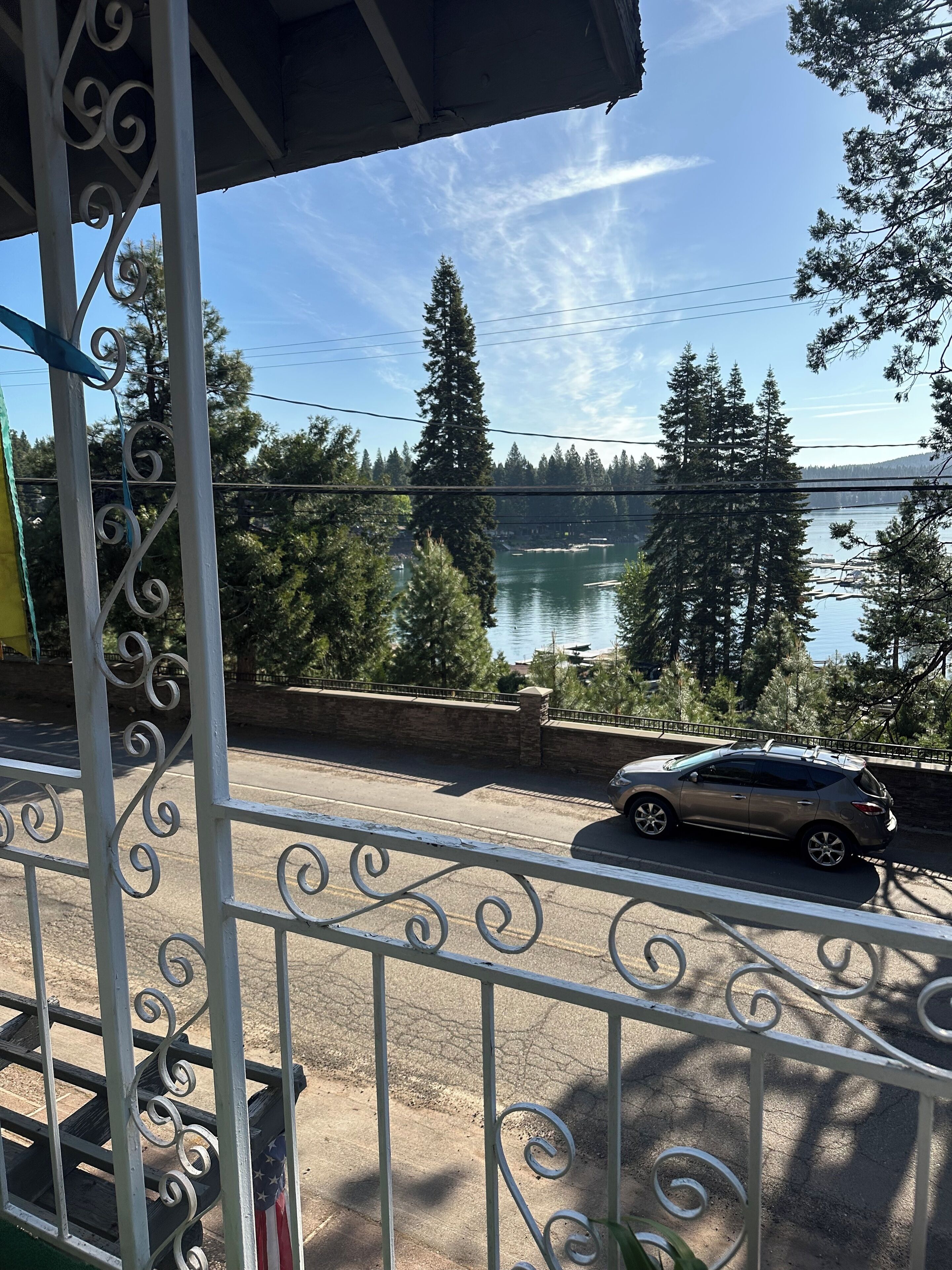 Ein Balkon mit Metallgeländer, der auf eine Straße mit Auto, einen See und Bäume blickt.