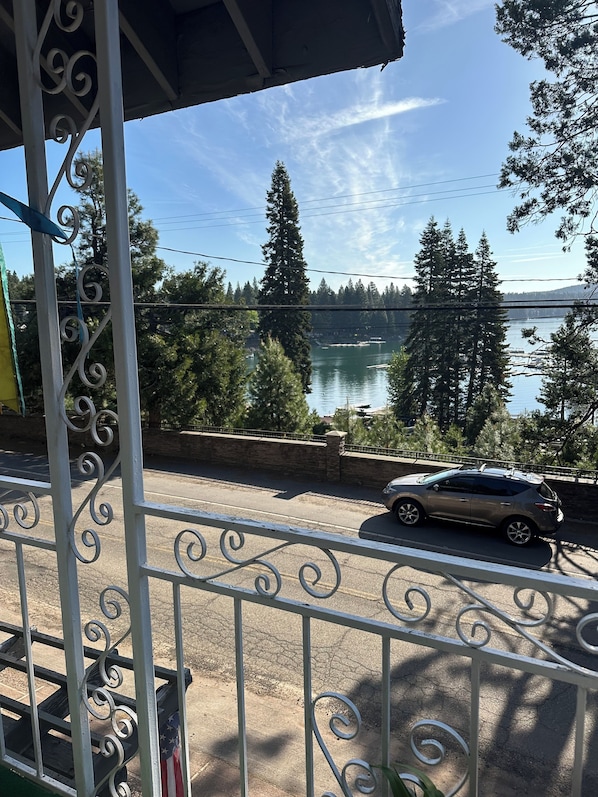 A balcony with a metal railing overlooking a road with a car, a lake, and trees. - House with 6 rooms each with private bath across street from lake! (Westwood)