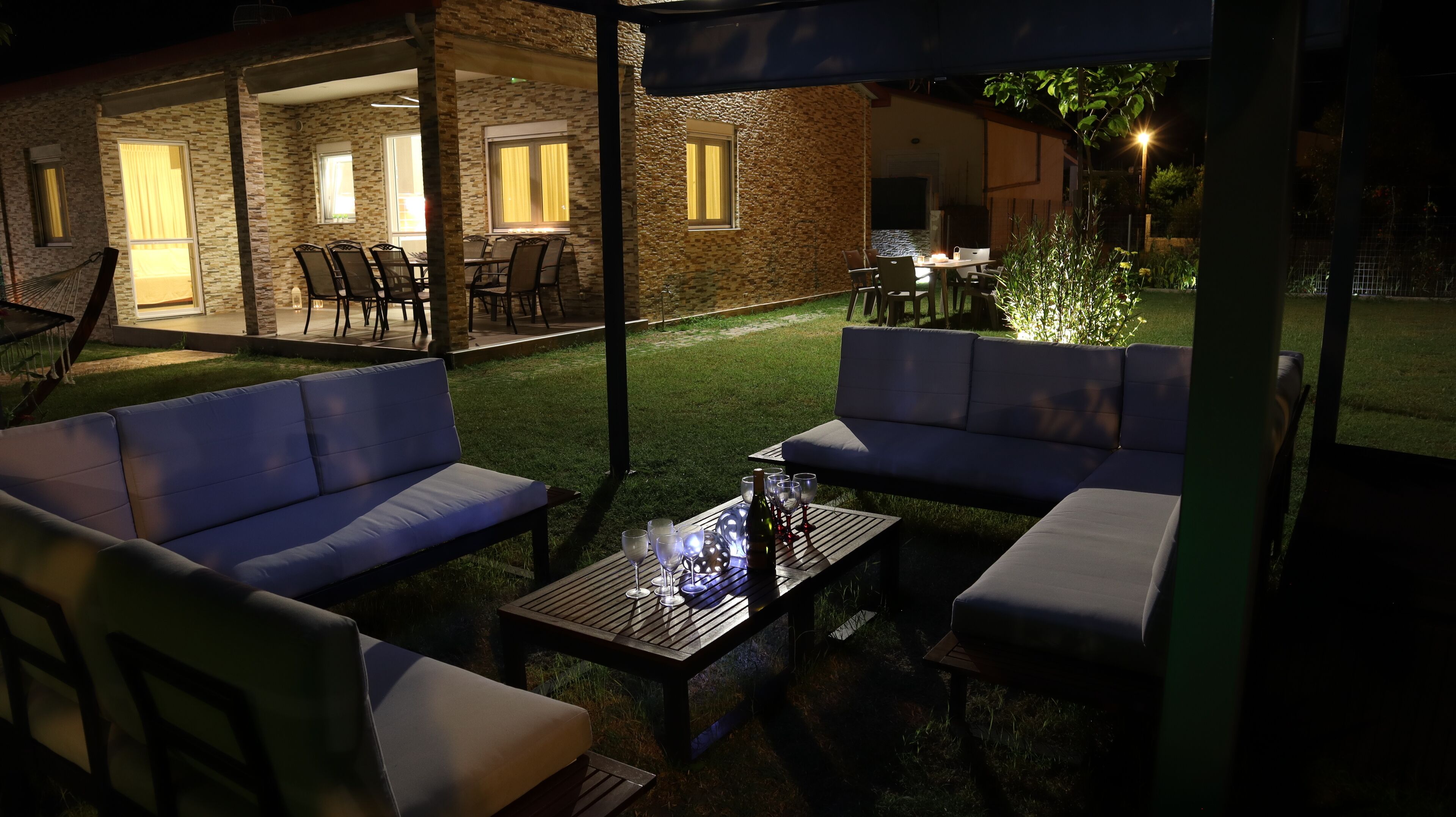 An outdoor patio with seating and a table, a bottle of wine, and glasses.