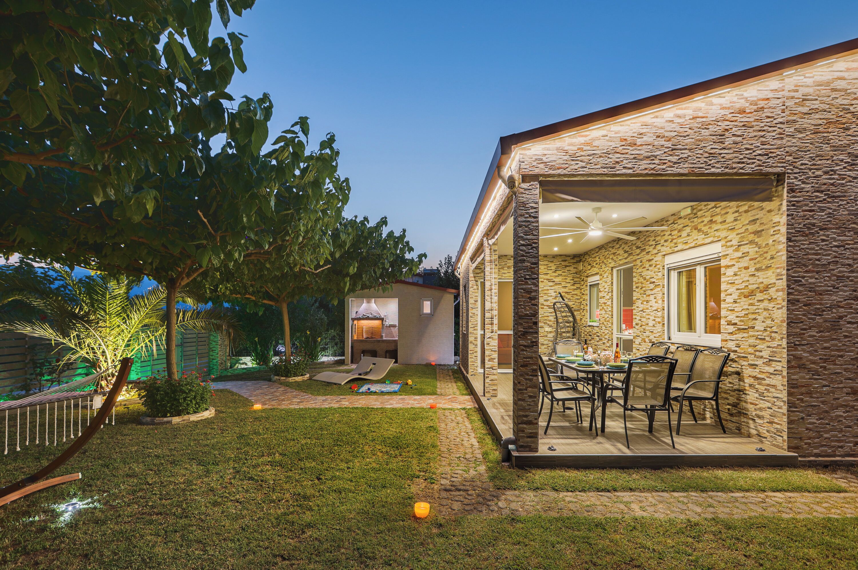 Un giardino sul retro con un muro in pietra, un barbecue e un'area pranzo con sedie.