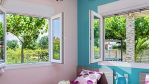 Un dormitorio con dos camas, ventilador de techo y ventanas amplias con vistas a la vegetación.
