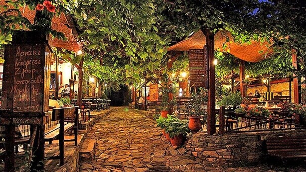 Un café al aire libre con suelo de piedra, mesas de madera y plantas en macetas.