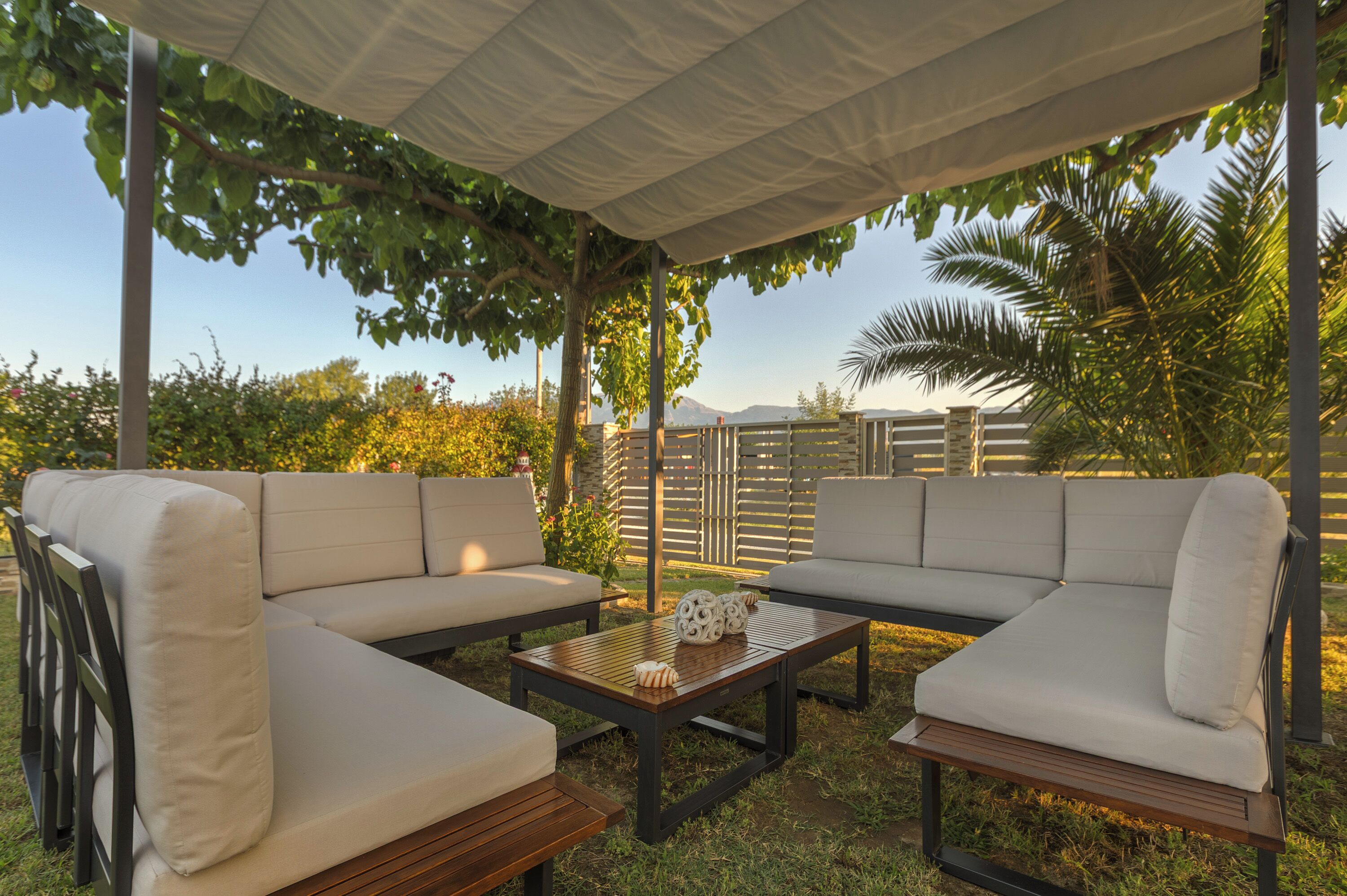An outdoor seating area with a covered patio, cushioned sofas, and a wooden coffee table.