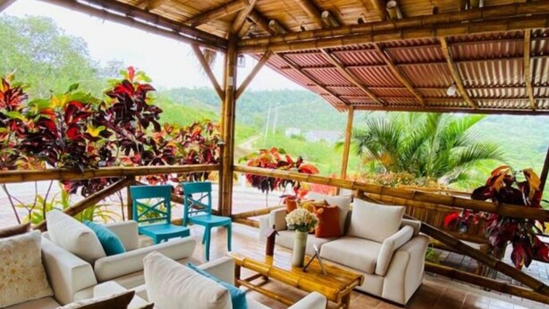 Ein überdachter Außenbereich mit weißen Sofas und Holzmöbeln, umgeben von üppiger Vegetation und Blick auf die Landschaft.