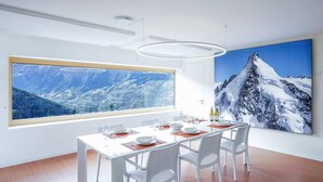 A dining area with a large window, white table, and chairs. - Exclusive architectural chalet at 1,600 metres, 4-6 pers. in impressive location (Suen)