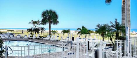 A pool area with lounge chairs and a view of the beach.