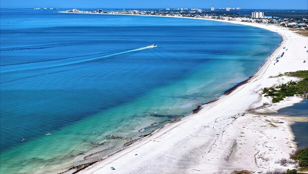 A coastal beach with clear turquoise waters, a sandy shore, and a distant cityscape. - Welcome to the paradises 
Departure clean included. Adv. #034724w10370b (Fort Myers Beach)