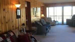 A cozy living room with wooden walls, a sofa, two armchairs, a lamp, and a view through large windows. - Montana Adventure (Dillon)