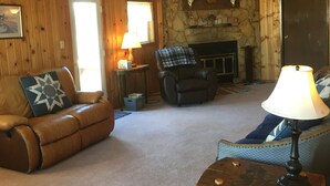 A cozy living room with a leather sofa, a blue armchair, a fireplace, and a stone wall. - Montana Adventure (Dillon)