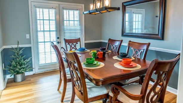 A dining area with a wooden table, six chairs, and a chandelier. - Suite 104 in Madison.... “Stay Awhile” (Madison)