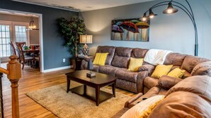 A living room with a brown leather sofa, a wooden coffee table, and a large floor lamp. There is a dining area in the background with a table and chairs. - Suite 104 in Madison.... “Stay Awhile” (Madison)