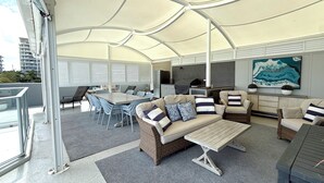 Ein überdachter Außenbereich mit Tisch und Stühlen, einer Couch und einem Fernseher.