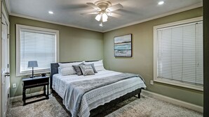 A bedroom with a bed, nightstand, lamp, ceiling fan, and a painting on the wall. - Relax in Shady Oaks Near Hospitals & Dining (Jackson)