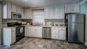 A modern kitchen with white cabinets, stainless steel appliances, and a marble floor. - Relax in Shady Oaks Near Hospitals & Dining (Jackson)