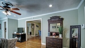 A spacious living room with hardwood flooring, a ceiling fan, a large wooden dresser with a mirror, and a television. - Relax in Shady Oaks Near Hospitals & Dining (Jackson)