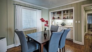 A dining area with a wooden table and blue chairs, a vase with red flowers, and a built-in cabinet with kitchen items. - Relax in Shady Oaks Near Hospitals & Dining (Jackson)