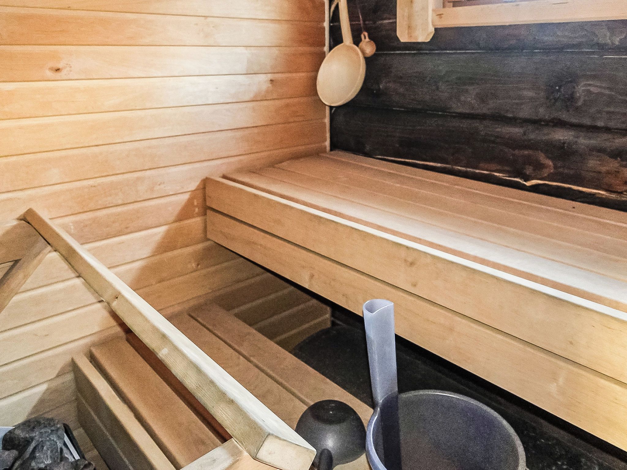 A sauna room with wooden benches and a black sauna floor.