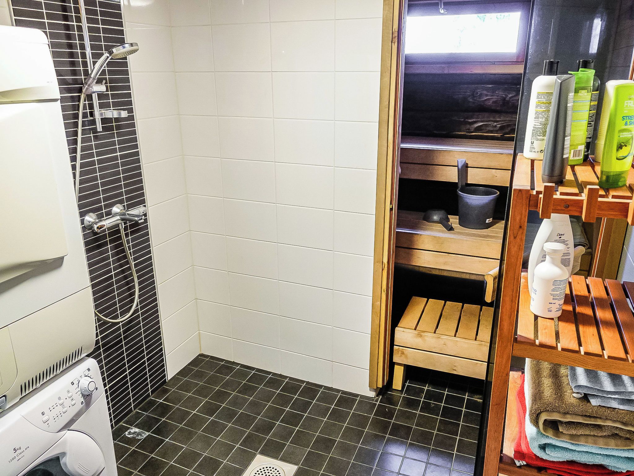 A compact bathroom with a shower, a drying rack, and a shelf with toiletries.