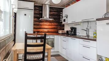 A compact kitchen with white cabinets, a wooden accent wall, a dining table with a chair, and a hanging light fixture.