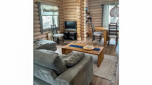 L'intérieur d'une cabane en rondins, avec un canapé, un téléviseur et un coin repas.