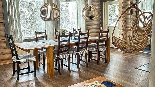 Un espace repas comprenant une table et des chaises en bois, des luminaires suspendus et une chaise en osier.