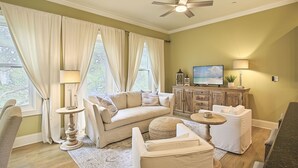 Una sala de estar con un sofá, un reposapiés y un televisor sobre un mueble de madera.