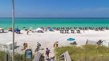 A beach with white sand, clear turquoise water, and several beach umbrellas.