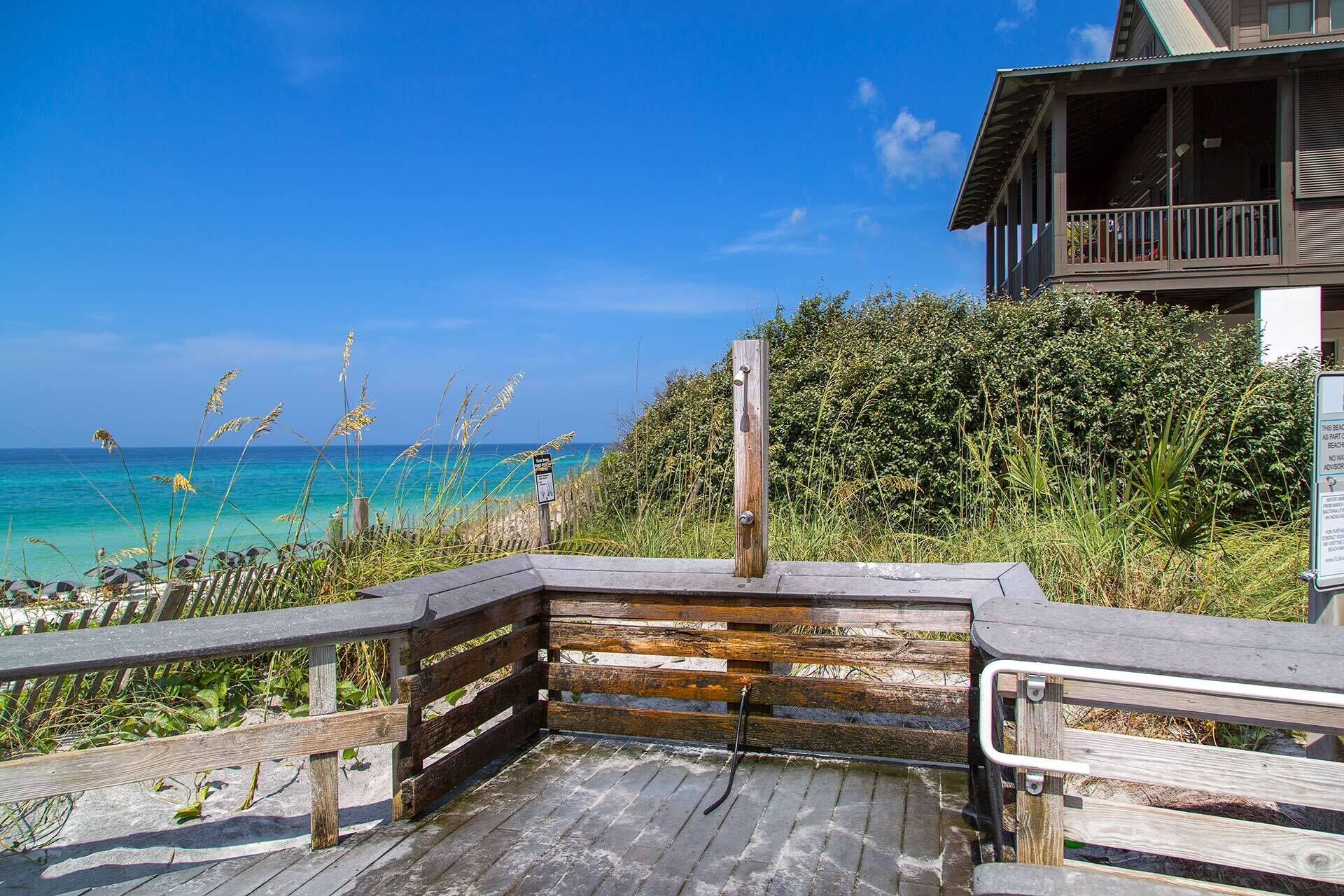 A wooden deck leading to a beach with a clear view of the ocean.