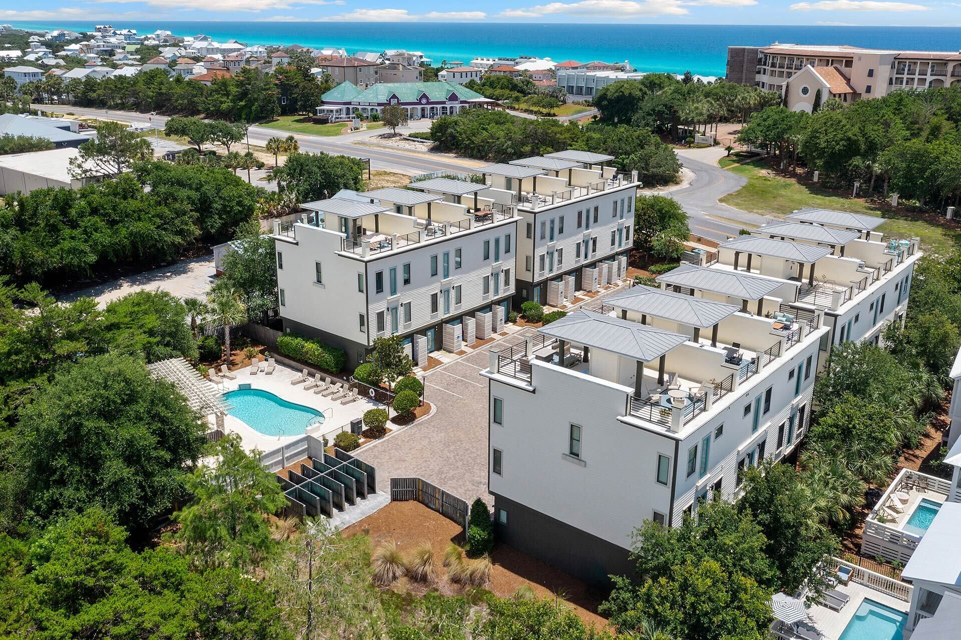 A modern apartment complex with multiple buildings, a swimming pool, and a view of the ocean.