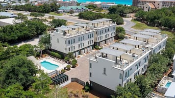 A modern apartment complex with multiple buildings, a swimming pool, and a view of the ocean.